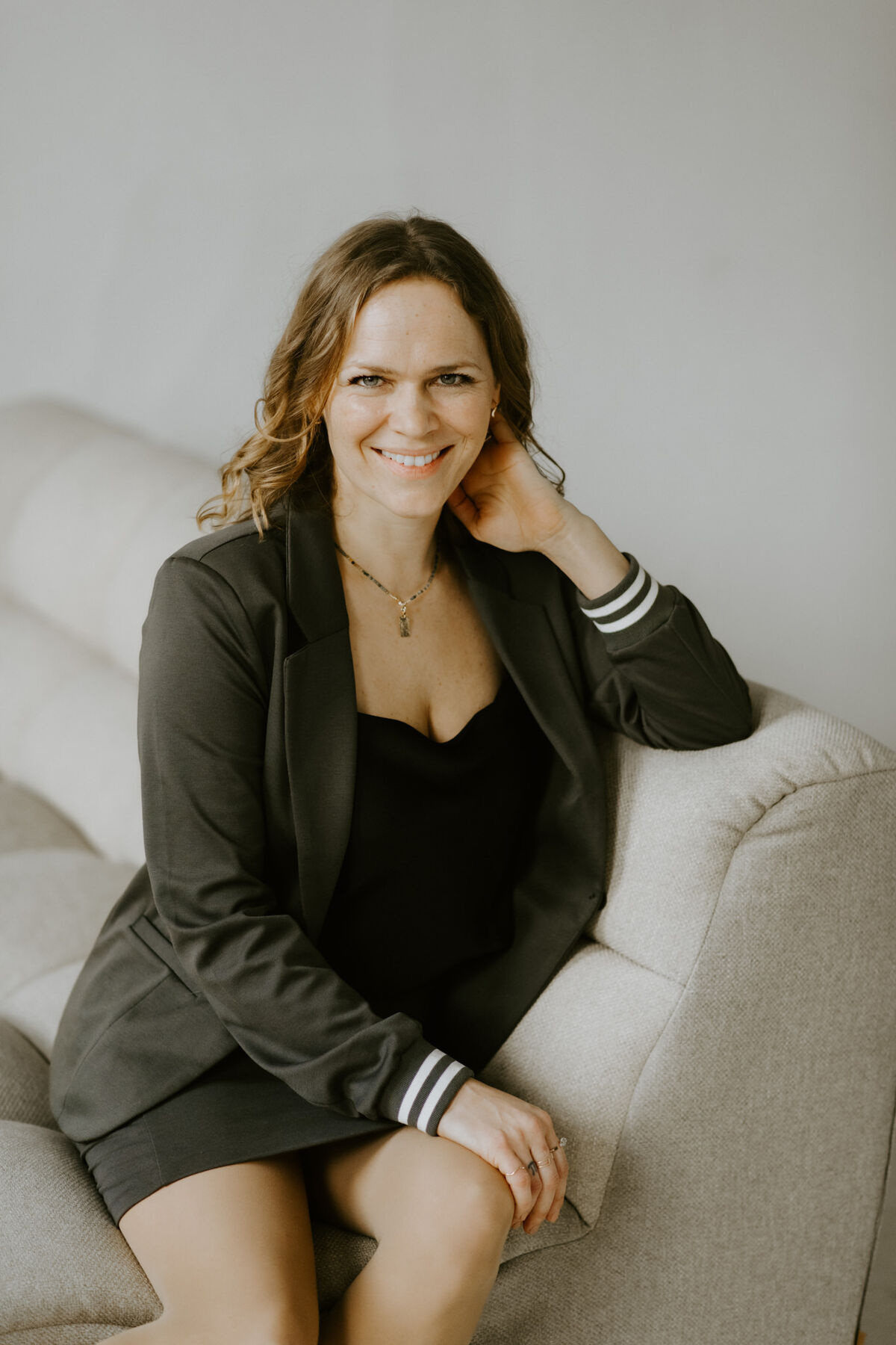 Raphaela Grollius sitzt lächelnd auf einem hellen Sofa